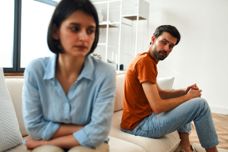 Unhappy sad couple sitting apart on couch in living room after quarrel, frustrated man and woman turning their back ignoring having conflict at home, can not find compromise, misunderstanding concept.