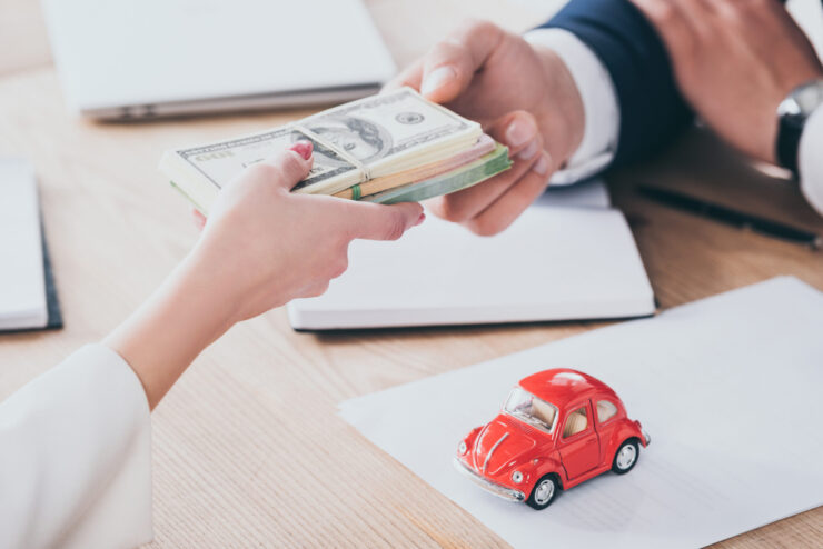 cropped shot of client giving money to businessman near red toy car on tabletop