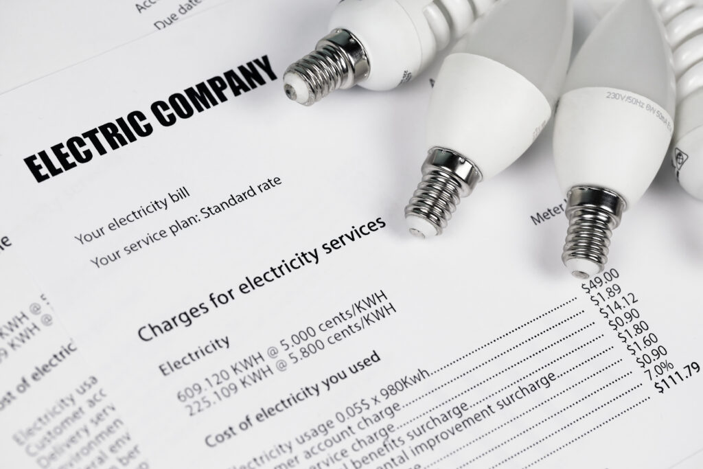 Electricity bill titled "Electric Company" with detailed charges and four white light bulbs on top. Emphasizes energy costs and usage.