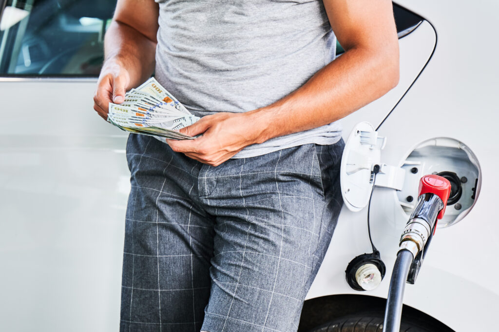 Man counting how much money he spending on fuel. Rising fuel prices concept. Cropped view of male counting dollars on background refueling car.