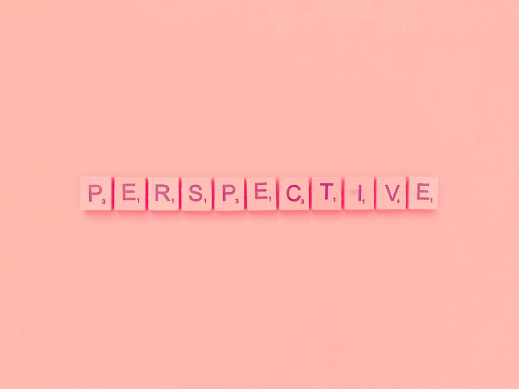 Pink Scrabble tiles spell "PERSPECTIVE" on a matching pink background. The tone is playful and creative.