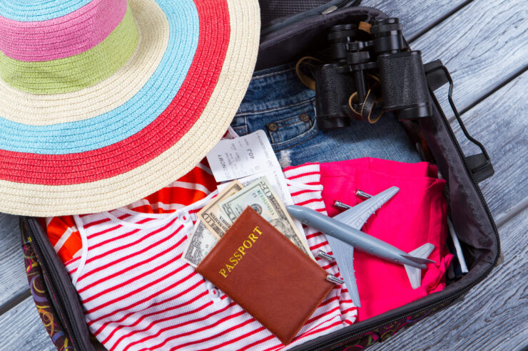 Open suitcase with a colorful hat, striped shirt, passport, money, plane ticket, and toy airplane, conveying a sense of excitement and travel readiness.