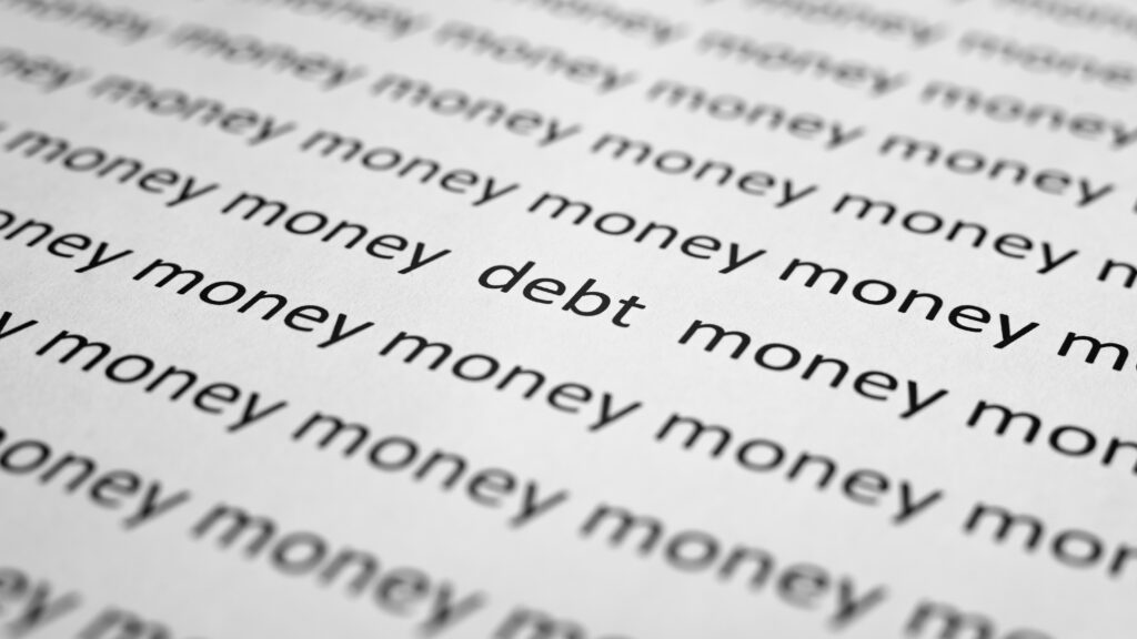 Rows of the word "money" in black text on white paper, with "debt" prominently interspersed. Conveys themes of financial stress and focus.