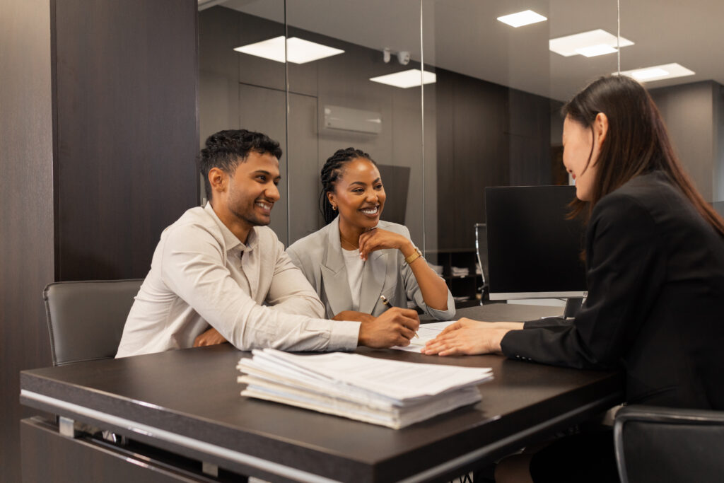 A smiling couple sits across a desk from a professional woman in an office setting, engaged in a positive discussion, with documents on the table.
