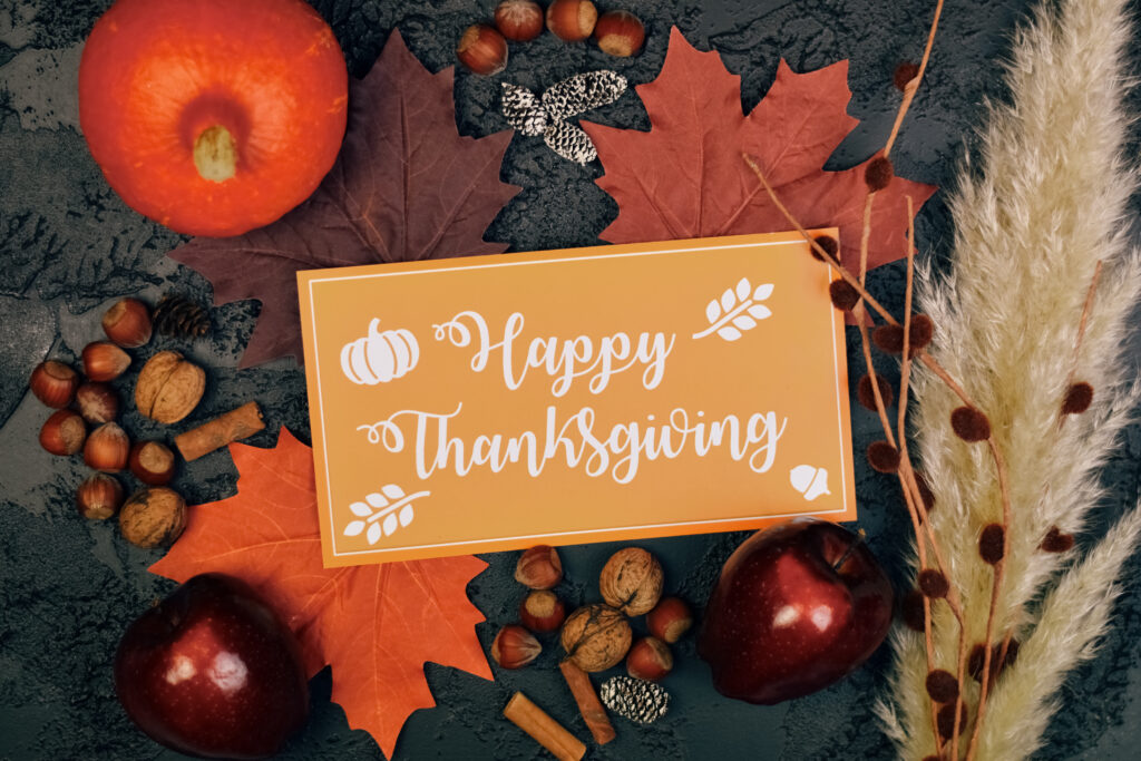 Autumn-themed flat lay with "Happy Thanksgiving" card, surrounded by pumpkins, apples, nuts, and leaves on a textured dark background.