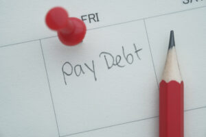 A colorful calendar note reminds to pay off debt, pinned with a red pushpin and pencil