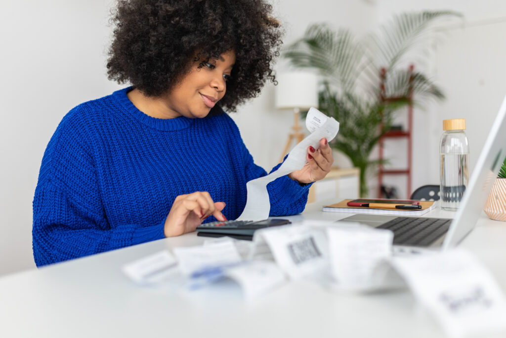 Young African American woman with a laptop computer managing budget and expenses bills at home.