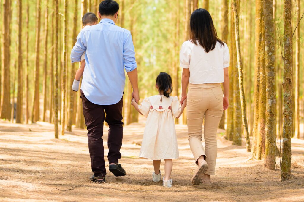 Happy family walking hand-in-hand through a sunlit forest trail, symbolizing the security and peace of mind achieved through debt relief options, helping families move forward debt free.