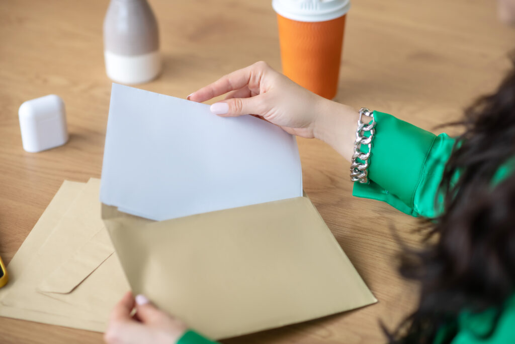 Woman opening a large envelope at a desk, revealing a document inside—possibly a debt validation letter.