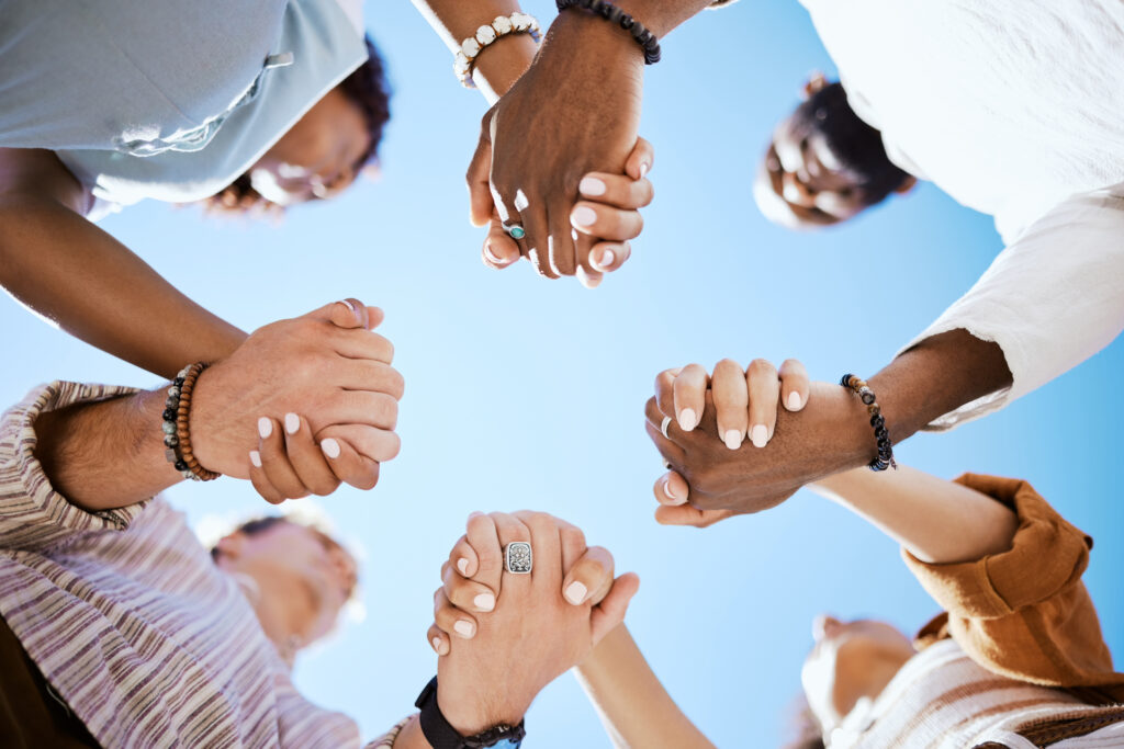 group holding hands in prayer or trust, viewed from below with an inspiring vantage of the blue sky