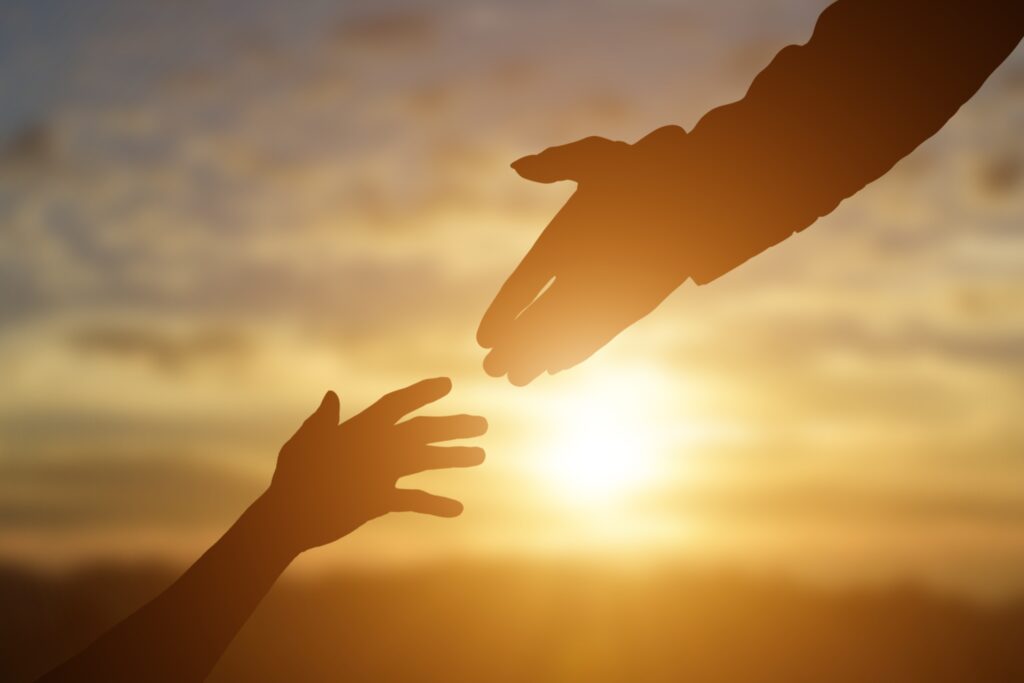 Silhouette of giving a helping hand, hope and support each other over sunset background.