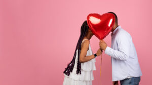 playful image of a young couple hiding behind their faces a heart balloon.