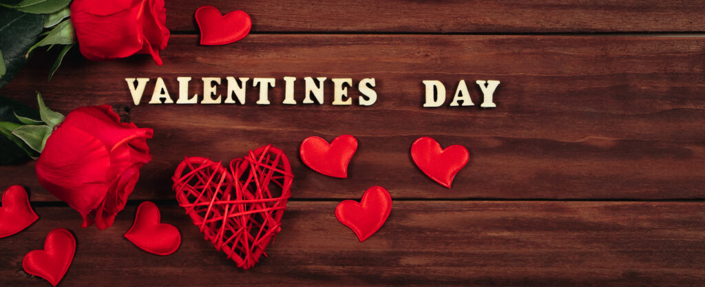 Gift boxes in craft paper and red roses on a wooden background. Valentine's day, place for text. Banner format