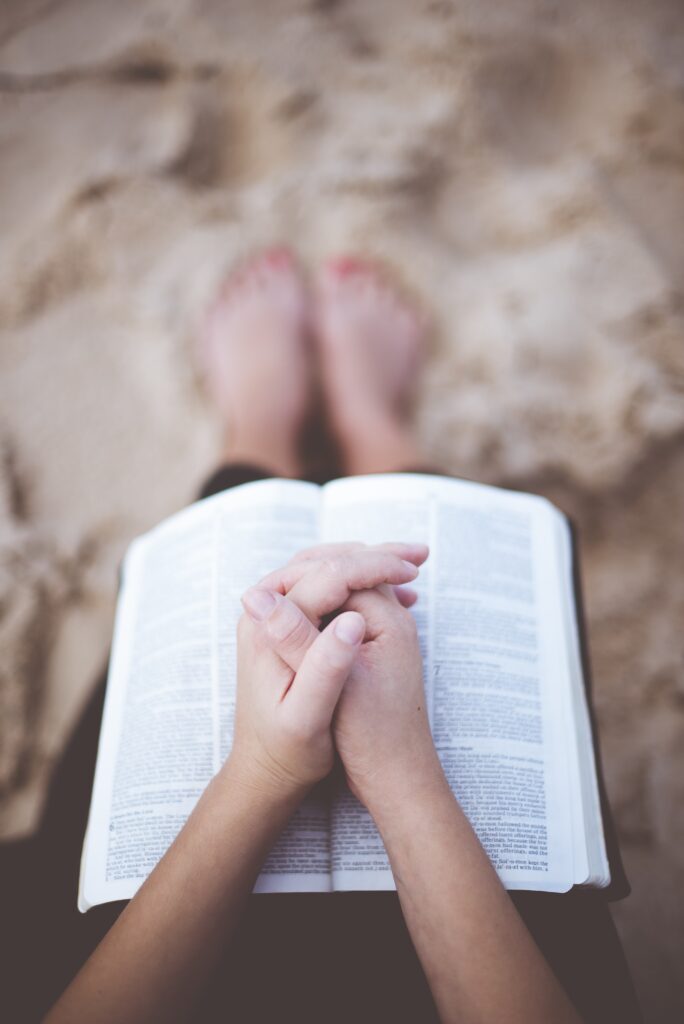 A vertical shot of a person praying with their hands on the bible