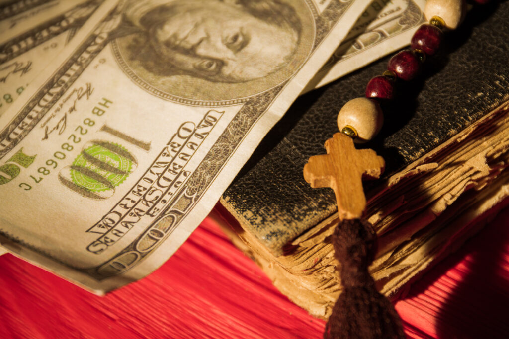 Close up old book, wooden cross on bead necklace and money. Religion and money concept.